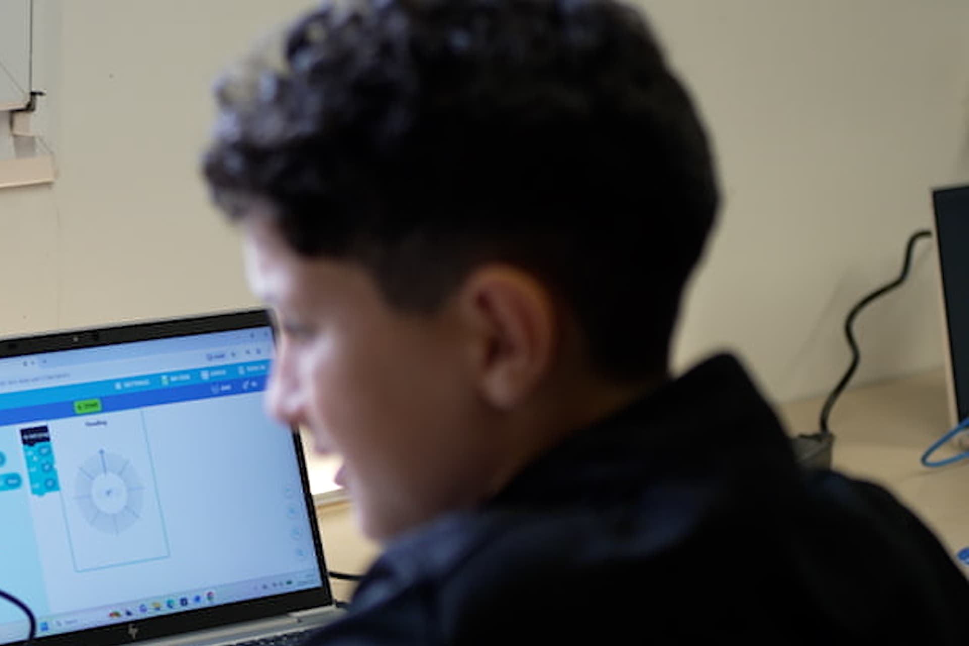 A boy at a laptop showing block-based code, seen from behind