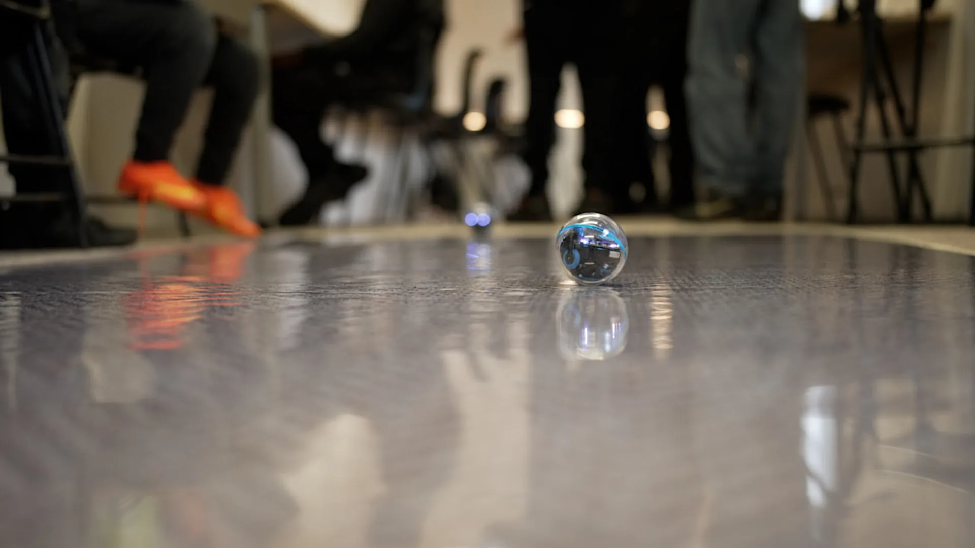 A Sphero robot rolling across the floor of the Hikora classroom, the class blurred behind it